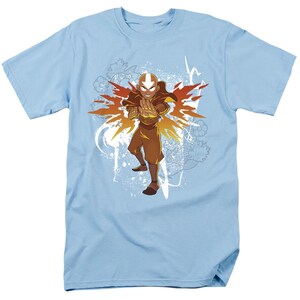 May include: A light blue t-shirt with a graphic of a cartoon character in a fiery orange and yellow explosion. The character is wearing a brown and orange outfit and has a white symbol on their forehead. The text "Avatar" is printed on the shirt.