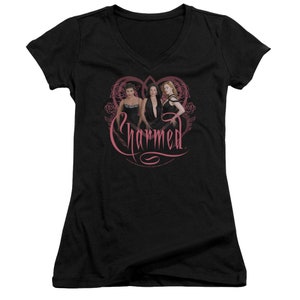 May include: Black v-neck t-shirt with a pink heart design featuring three women in black dresses and the text "Charmed" in pink.