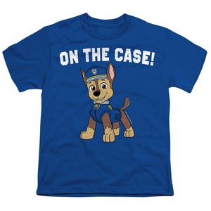 May include: A blue t-shirt featuring a cartoon image of Chase from Paw Patrol. The character is wearing a police uniform and hat. The text "ON THE CASE!" is printed above the character in white.
