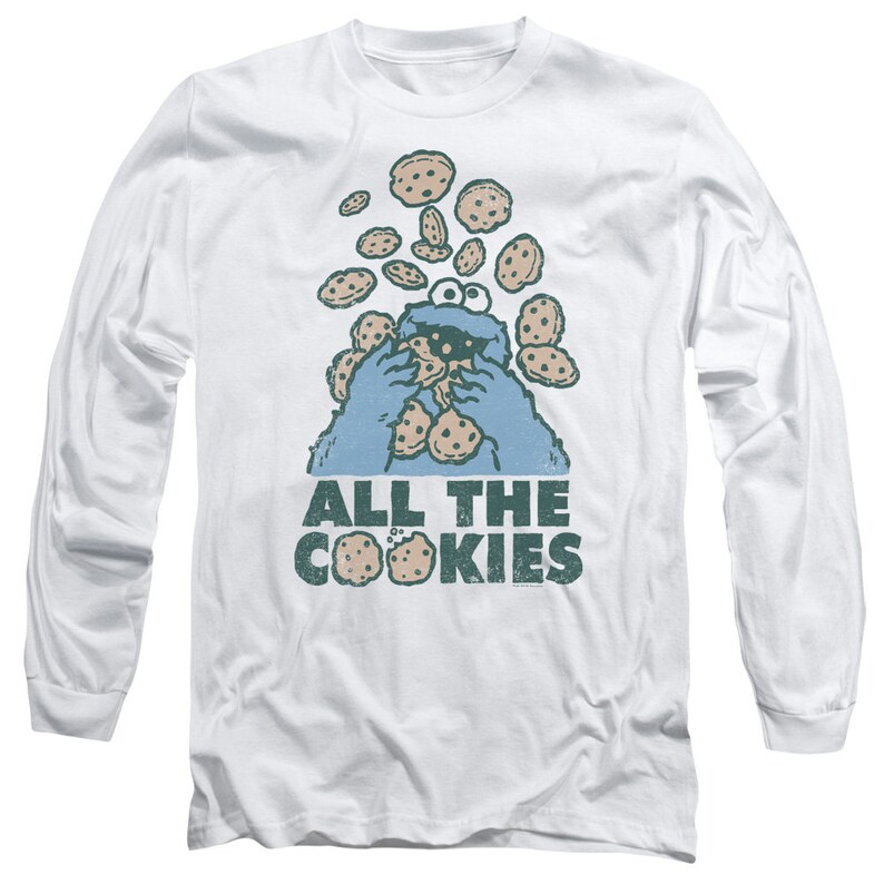 May include: A white long-sleeved t-shirt with a blue Cookie Monster character eating cookies. The text "All the Cookies" is printed below the character.