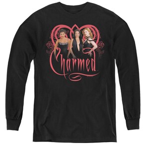 May include: Black long-sleeve t-shirt with a pink graphic of three women in black dresses standing in front of a pink heart with the word "Charmed" written in pink.