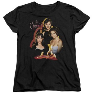 Puede incluir: Camiseta negra con un gr&aacute;fico de los tres personajes principales del programa de televisi&oacute;n "Charmed" con el t&iacute;tulo del programa en una fuente estilizada. Los personajes est&aacute;n de pie frente a un libro en llamas.