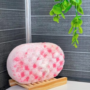 A Soap Infused Sponge after being used. It is set on a drying rack on the side of the bath tub, still covered in some soapy bubbles. These sponges can be used daily for up to three weeks while still retaining soap and a great fragrance. They just need to be set down to dry after use, and then they are ready to use again.