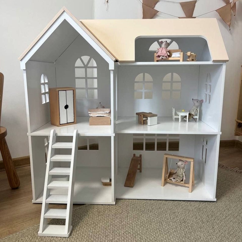Op de afbeelding: Een wit houten poppenhuis met een lichtbeige dak en meerdere kamers. Het poppenhuis heeft een ladder, een schommel en miniatuurmeubels, waaronder een bed, tafel, stoelen en een kledingkast. Kleine muizenfiguren zijn door het hele huis geplaatst.