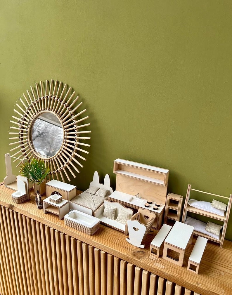 Puede incluir: Un conjunto de muebles de madera en miniatura para una casa de mu&ntilde;ecas, que incluye una cama, una cocina, una litera, una mecedora, una mesa y una mesita de noche. Los muebles est&aacute;n pintados de blanco y tienen un acabado de madera natural. Los muebles est&aacute;n dispuestos en un estante de madera con una pared verde en el fondo.