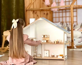 May include: A wooden dollhouse with a white exterior, gray roof, and miniature furniture. The dollhouse has two stories, a ladder, and a small balcony. The interior is visible, with tiny beds, tables, and chairs. The dollhouse is on a wooden floor.