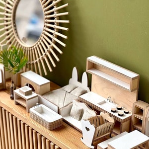 Puede incluir: Un conjunto de muebles en miniatura para casa de mu&ntilde;ecas hecho de madera con un acabado blanco. El conjunto incluye una cama, un sof&aacute;, una ba&ntilde;era, un fregadero de cocina, una cuna y un estante. Los muebles est&aacute;n dispuestos sobre una mesa de madera con un dise&ntilde;o de listones.