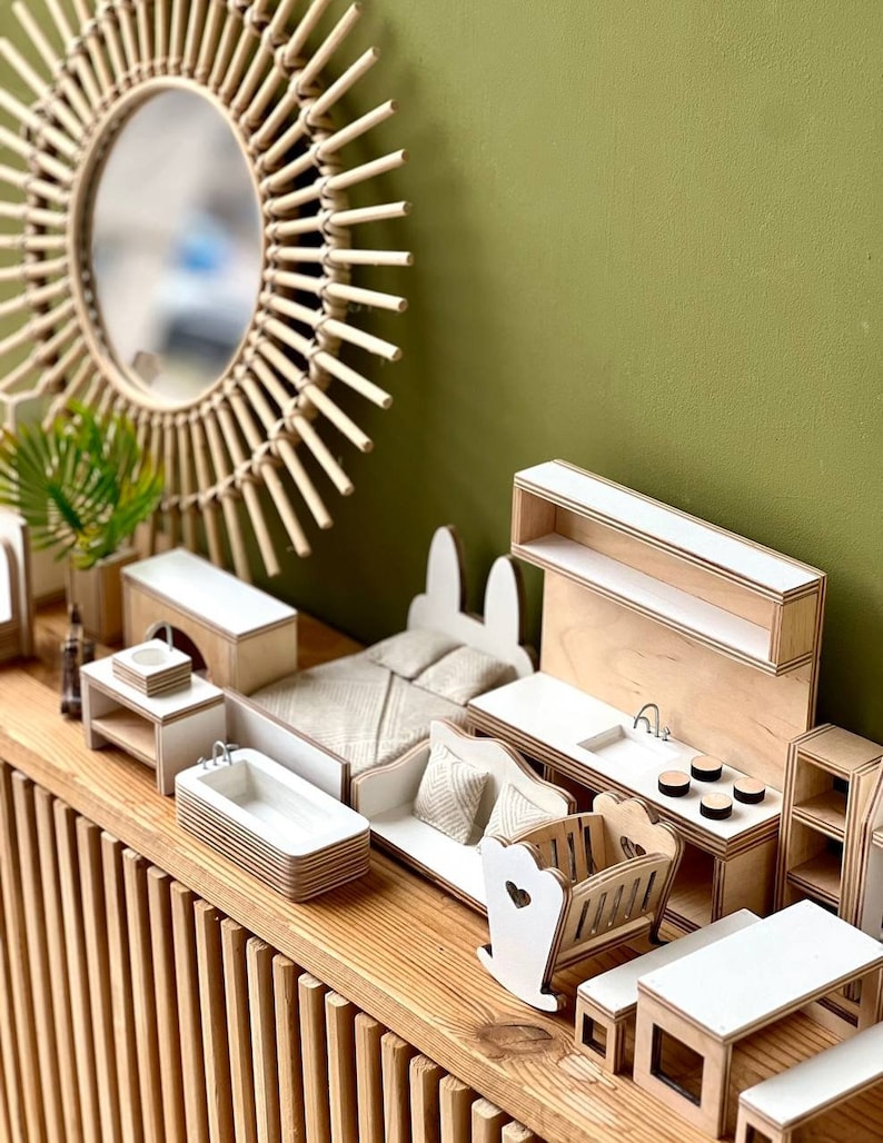 Puede incluir: Un conjunto de muebles en miniatura para casa de mu&ntilde;ecas hecho de madera con un acabado blanco. El conjunto incluye una cama, un sof&aacute;, una ba&ntilde;era, un fregadero de cocina, una cuna y un estante. Los muebles est&aacute;n dispuestos sobre una mesa de madera con un dise&ntilde;o de listones.
