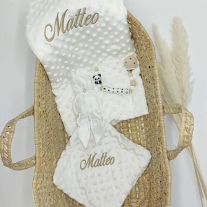 Peut inclure: Une couverture de bébé blanche avec le nom "Matteo" brodé dessus. La couverture est dans un panier en osier avec un lapin en peluche blanc et un jouet en perles de bois avec un charme panda.