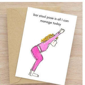 May include: A greeting card with a watercolor illustration of a person in a yoga pose. The person is wearing pink pants and a pink top. The card reads "bar stool pose is all I can manage today."