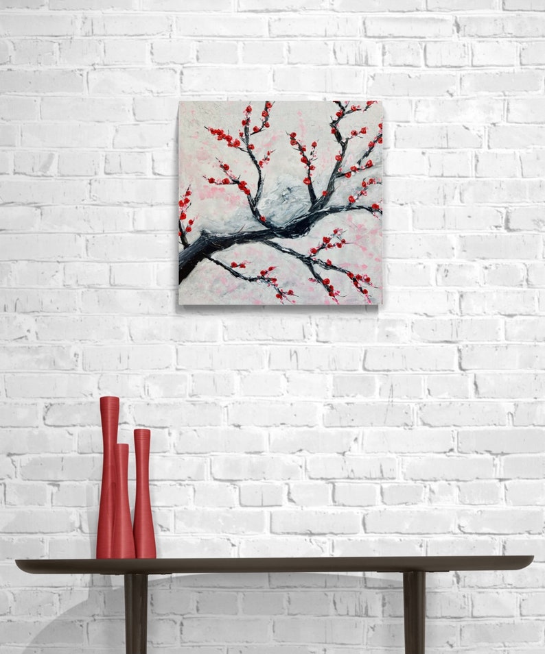 Op de afbeelding: Een schilderij van een gestileerde tak met rode bloemen op een witte achtergrond. De tak is zwart geschilderd en de bloemen zijn felrood.
