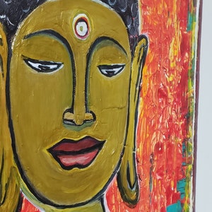 May include: A painting of a Buddha with a golden face and a red background. The Buddha has a third eye on his forehead and is wearing a red robe.