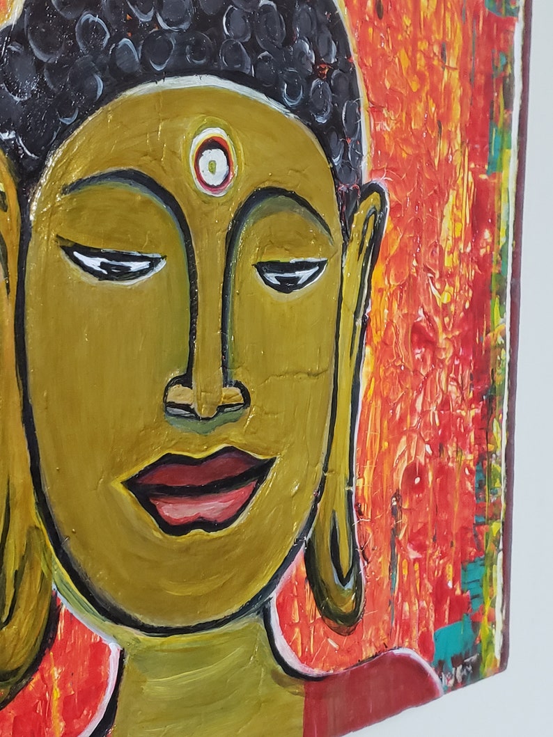 May include: A painting of a Buddha with a golden face and a red background. The Buddha has a third eye on his forehead and is wearing a red robe.