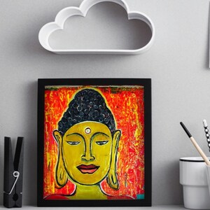 May include: A framed painting of a Buddha with a yellow face, black hair, and a red and orange background.