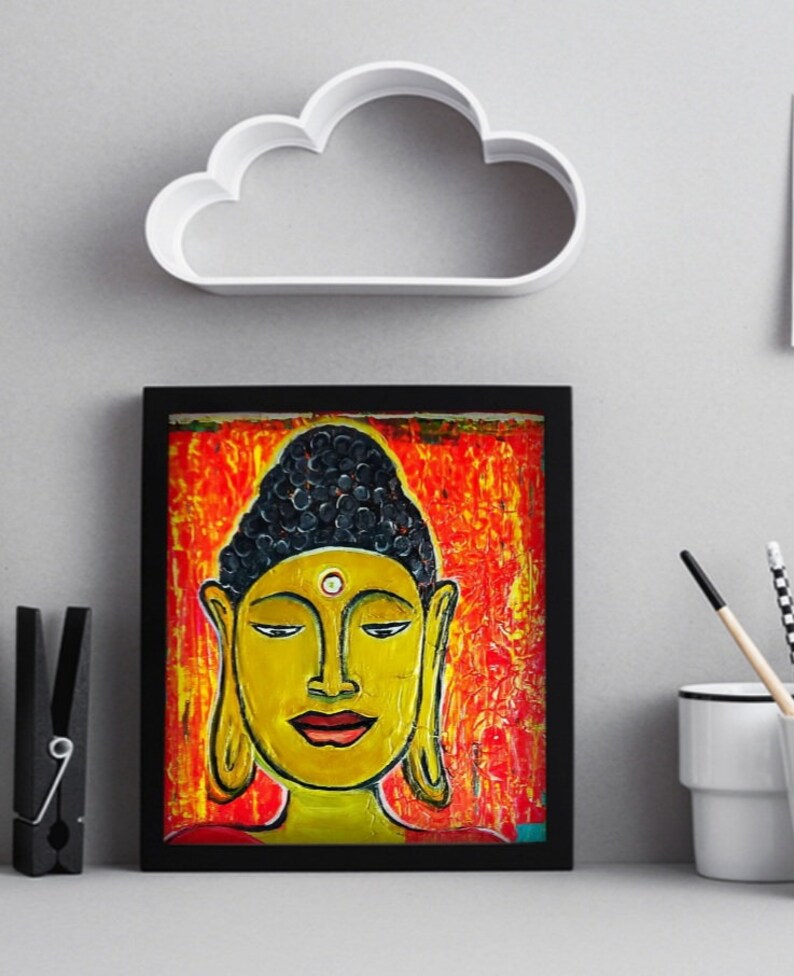 May include: A framed painting of a Buddha with a yellow face, black hair, and a red and orange background.