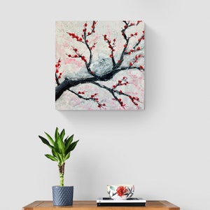 Op de afbeelding: Een schilderij van een zwarte tak met rode bloemen tegen een witte en roze achtergrond.