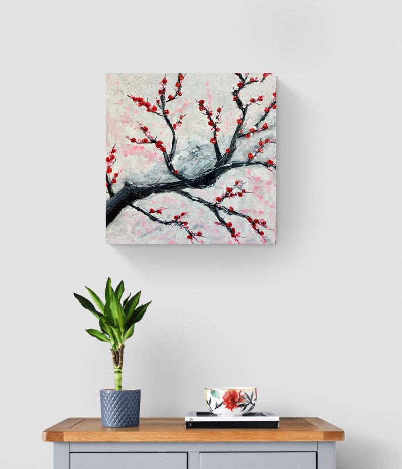 Op de afbeelding: Een schilderij van een zwarte tak met rode bloemen tegen een witte en roze achtergrond.