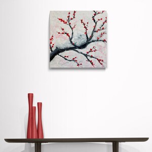 Op de afbeelding: Een schilderij van een witte en grijze tak met rode bloemen. Het schilderij is op een witte achtergrond en is ingelijst in een zwart frame.