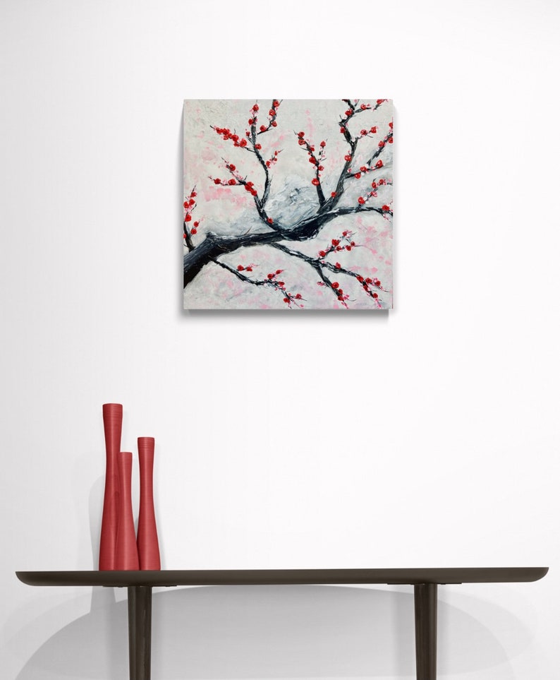 Op de afbeelding: Een schilderij van een witte en grijze tak met rode bloemen. Het schilderij is op een witte achtergrond en is ingelijst in een zwart frame.