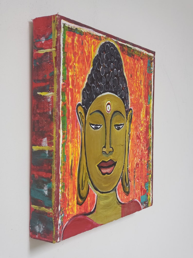May include: A painting of a Buddha with a red, orange, and yellow background. The Buddha has a black bun and a white dot on their forehead.