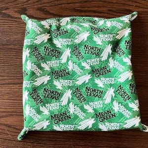 Puede incluir: Bolsa de tela verde con un patrón repetido blanco y negro de las palabras "Mean Green" y "North Texas".