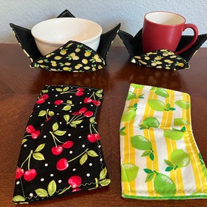 May include: Four fabric bowl and mug cozies. Two cozies are black with white polka dots and a red cherry pattern. Two cozies are black with yellow stripes and a green lemon pattern.