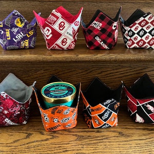 May include: Eight fabric bowl cozies in various patterns and colours, including purple, red, black, and orange. Some cozies feature college team logos and text. One cozy holds a container of ice cream.