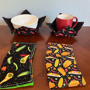 May include: Two black fabric bowl and mug cozies with red chili pepper designs. Two additional cozies with black backgrounds and green chili peppers, corn, and tacos designs.