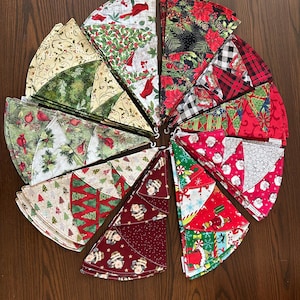 May include: A collection of Christmas tree skirts in various festive patterns. Designs include cardinals, holly, poinsettias, plaid, and Santa Claus. The skirts are arranged in a circular pattern on a wooden surface.