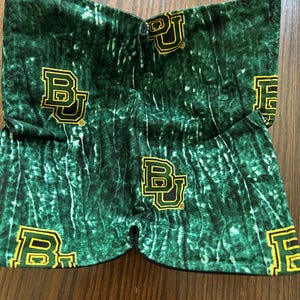 May include: Green fabric with a white and green camouflage pattern. The fabric has a repeated pattern of the letters "BU" in yellow.