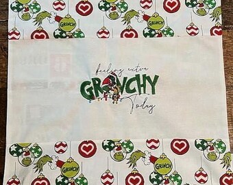 Peut inclure: Un coussin en tissu blanc avec un motif vert du Grinch. Le coussin a un cœur rouge et des ornements verts et blancs. Le texte "feeling extra GRINCHY today" est imprimé sur le coussin.