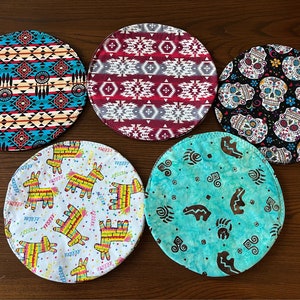 May include: Six round fabric coasters with different colourful patterns. The coasters feature designs of a pinata, a skull, a bear paw print, and geometric patterns.