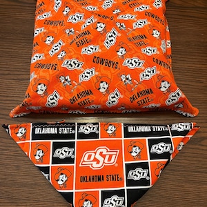 May include: Orange and black fabric pillow and bandana with the Oklahoma State University logo and the words "Oklahoma State" and "Cowboys".