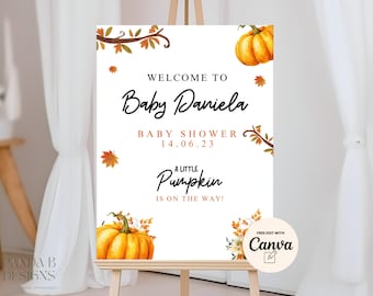 May include: A white welcome sign with fall-themed decorations, including pumpkins and leaves. The text reads "Welcome to Baby Daniela Baby Shower 14.06.23 A Little Pumpkin Is On The Way!" and includes a logo for Canva.