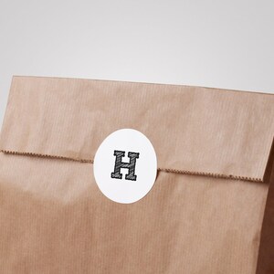 May include: A brown paper bag with a white circle sticker that has a black letter "H" inside.