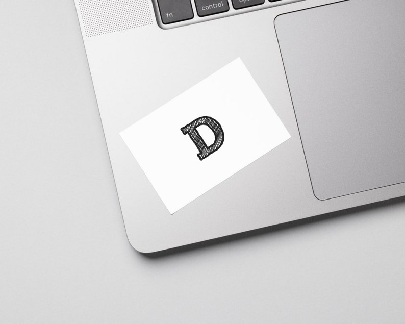 May include: A white sticker with a black, hand-drawn letter "D" on a silver laptop.