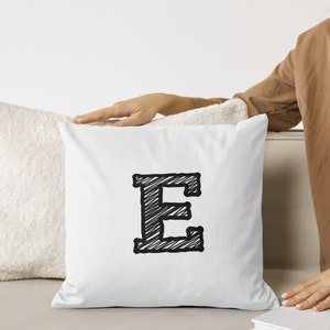 May include: White throw pillow with a black and white sketched letter E in the center.