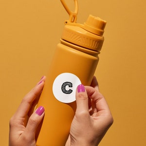 May include: A yellow water bottle with a white sticker that says "C" on it. The bottle is being held by a person's hands.