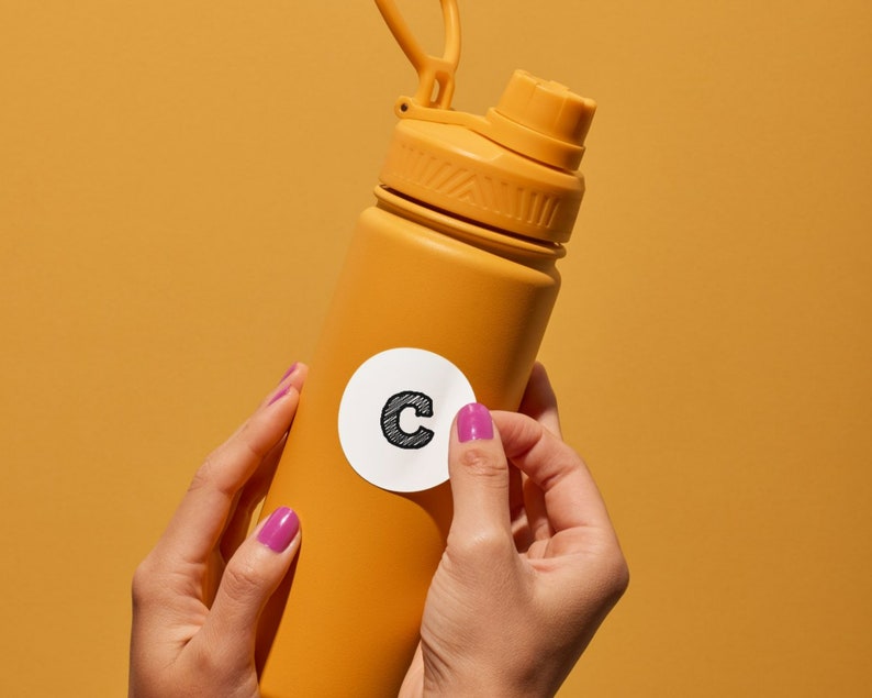 May include: A yellow water bottle with a white sticker that says "C" on it. The bottle is being held by a person's hands.