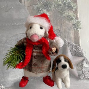 May include: A needle-felted mouse figurine wearing a red and white Santa hat, a red scarf, and a brown plaid coat with red shoes, holding a small green pine branch, standing next to a small needle-felted dog with brown and white fur.