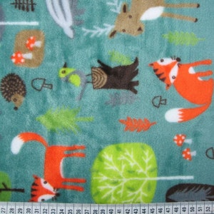 May include: Teal blue fabric with a repeating pattern of woodland animals, including foxes, deer, birds, hedgehogs, mushrooms, and trees. The fabric has a soft, fuzzy texture.