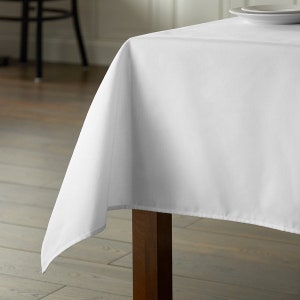 May include: A white tablecloth draped over a wooden table. The tablecloth is smooth and wrinkle-free, with a slight sheen.