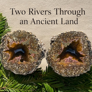 May include: Two circular geode halves featuring brown, gold, and purple crystalline interiors with a central hollow. The text "Two Rivers Through an Ancient Land" is printed above the stones, which are surrounded by green evergreen needles.