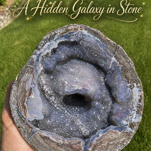May include: A geode with a sparkling, crystalline interior in shades of gray and blue. The outer shell is a mix of gray and brown. The text "A Hidden Galaxy in Stone" is arched above the geode.