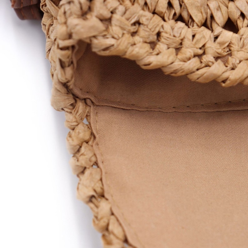 May include: Close-up of a woven straw bag with a light brown fabric lining. The bag's exterior is made of tightly woven straw, creating a textured surface. The interior lining is a solid, light brown fabric.