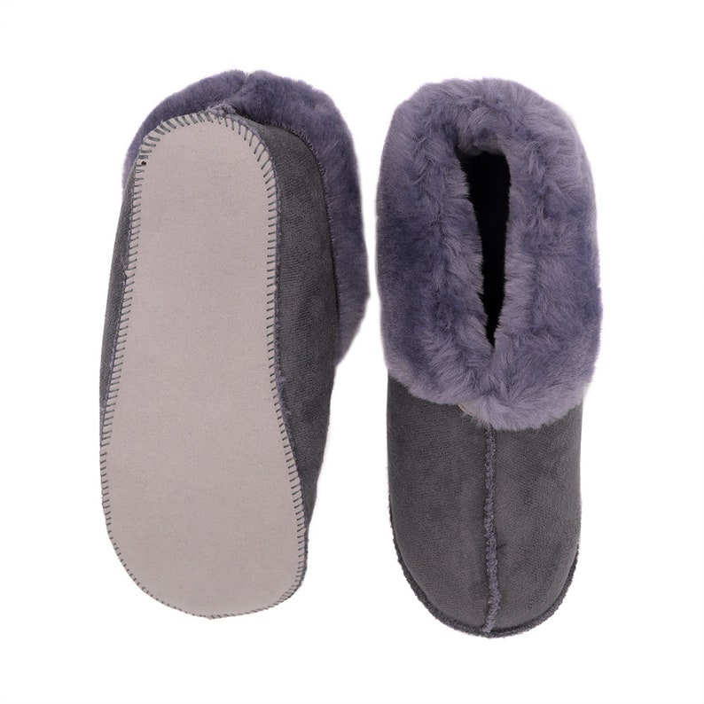 Op de afbeelding: Een paar grijze su&egrave;de pantoffels met een zachte, pluche voering. De pantoffels hebben een gesloten neus en een platte zool.