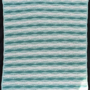 May include: A rectangular, handmade crochet blanket with a wavy pattern. The blanket features alternating horizontal stripes of white and teal blue. The texture of the crochet stitches is visible, creating a soft, textured appearance. The blanket is likely made of soft yarn.