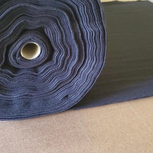 May include: A roll of black fabric is lying on a wooden surface. A pair of silver scissors is lying on the fabric.