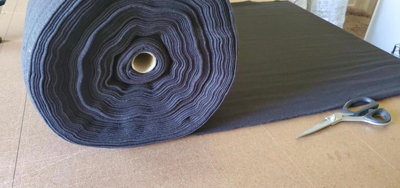 May include: A roll of black fabric is lying on a wooden surface. A pair of silver scissors is lying on the fabric.