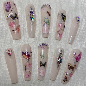 Pu&ograve; includere: Un set di dieci unghie finte lunghe a forma di bara. Ogni unghia &egrave; rosa pallido con decalcomanie di farfalle e fiori. Alcune unghie presentano strass iridescenti e dettagli a catena argentata. Le farfalle sono in vari colori.